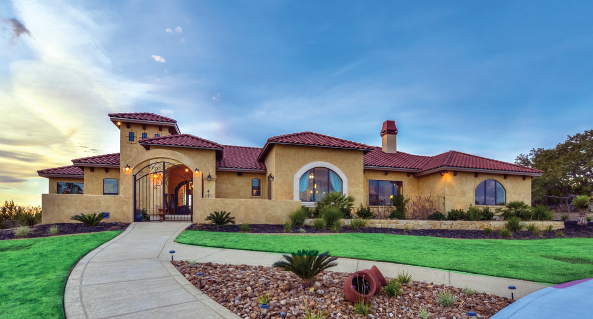 A picturesque Mediterranean-style house featuring a tiled roof, arched windows, and a welcoming pathway through manicured landscaping.